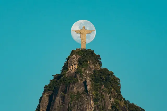The Christ the Redeemer statue on Corcovado with its arms outstretched against the sky beside the moon