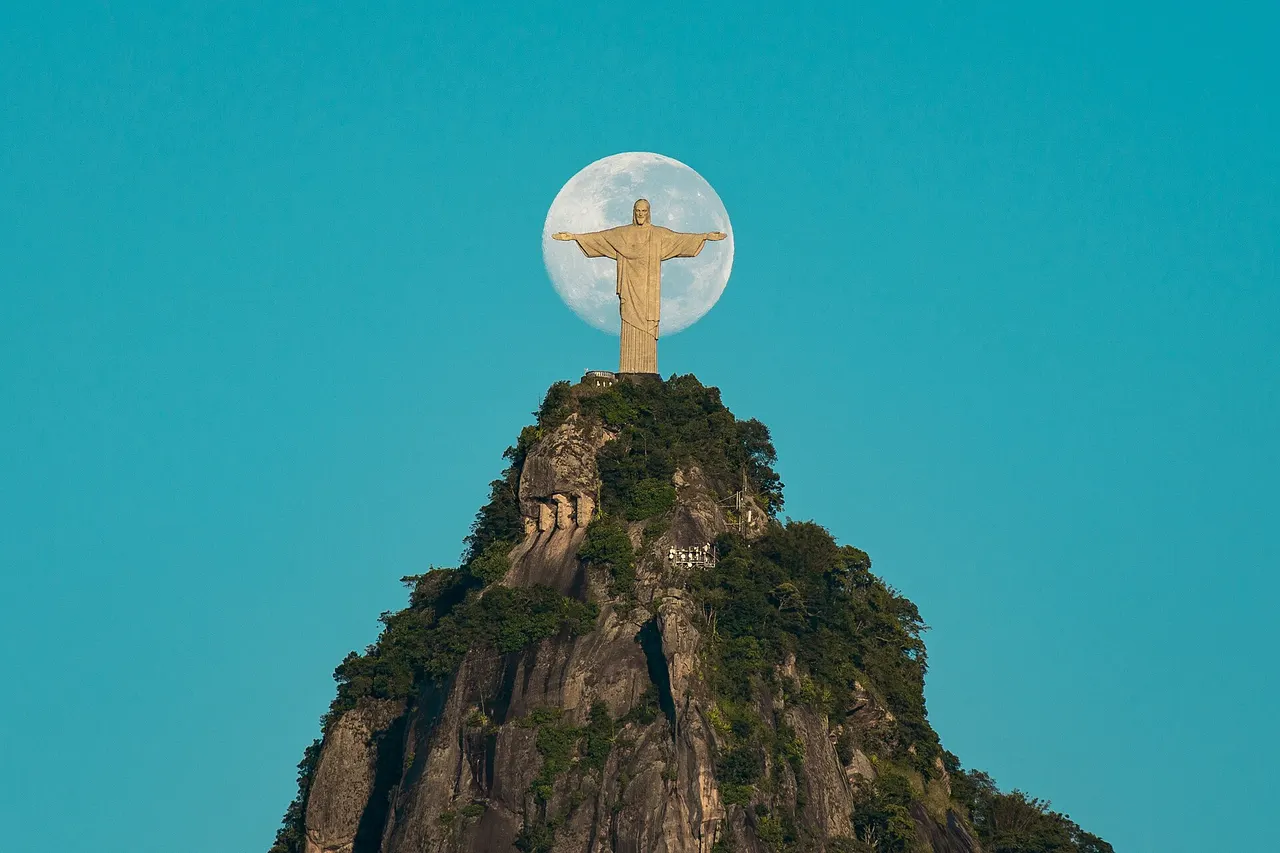 The Christ the Redeemer statue on Corcovado with its arms outstretched against the sky beside the moon