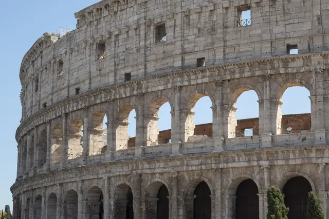 The tiered stone arches of the Colosseum's outer wall in Rome under a blue sky