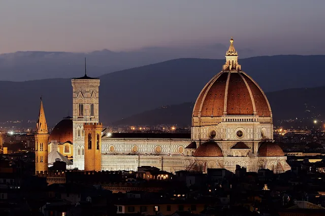 The red-tiled dome of Florence Cathedral and Giotto's bell tower lit up at dusk above the city rooftops