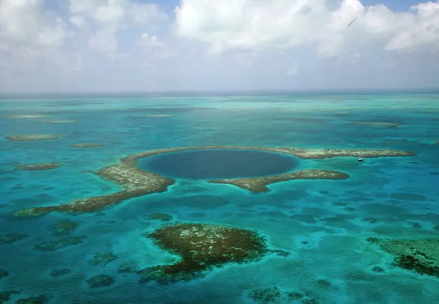 Aerial view of the dark circular Great Blue Hole surrounded by turquoise shallows on Lighthouse Reef
