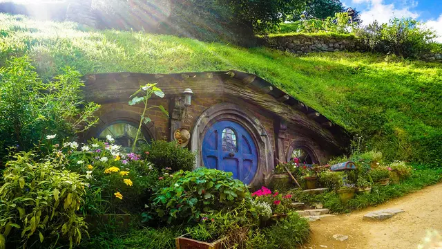 A hobbit hole with a round blue door set into a grassy hillside, surrounded by flowers at the Hobbiton Movie Set