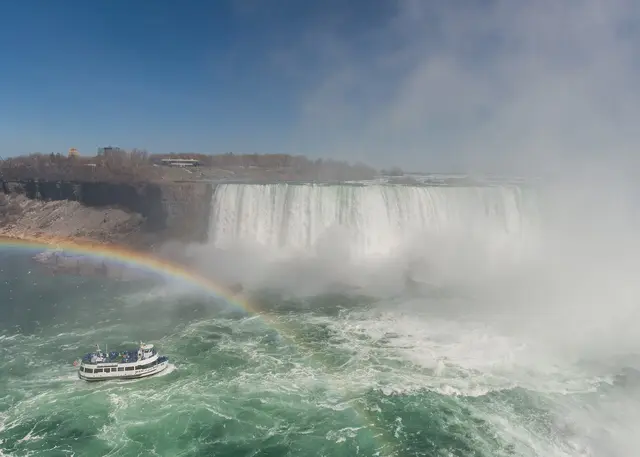 A tour boat approaching the mist and spray at the foot of the Horseshoe Falls, with a rainbow over the water