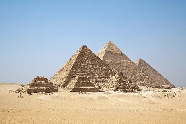 The pyramids of Giza in a row with three smaller queens' pyramids in front, under a clear blue sky