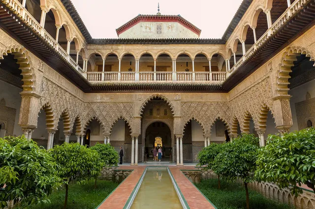 The long reflecting pool of the Patio de las Doncellas framed by carved arches and orange trees in the Real Alcázar of Seville