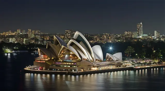 The Sydney Opera House lit up at night on Bennelong Point, with the city skyline behind