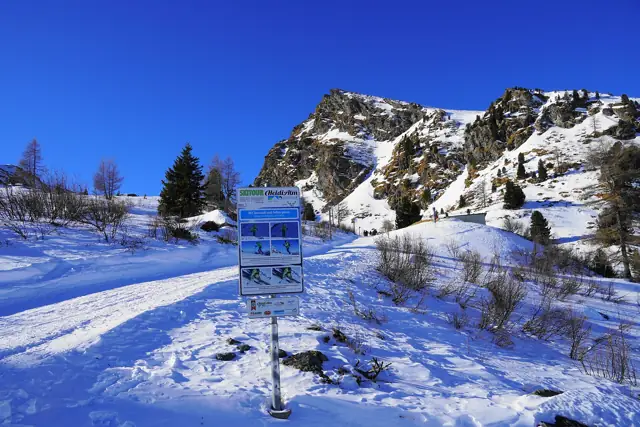 A gentle snow-covered slope with a piste sign under blue skies at the Heidi Alm ski area in the Nockberge mountains, Carinthia, Austria