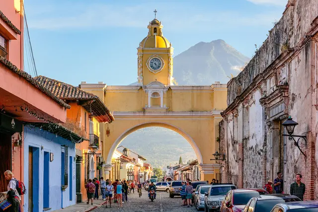 The yellow Santa Catalina Arch over a cobbled street in Antigua Guatemala, with a volcano behind