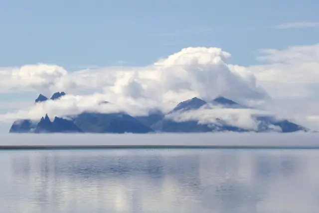 The jagged Vestrahorn mountain wrapped in cloud above a calm, reflective lagoon, seen from Iceland's Ring Road in the south-east