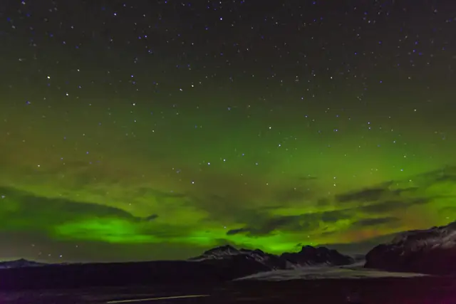 Green northern lights swirling across a starry night sky over a dark landscape in Iceland