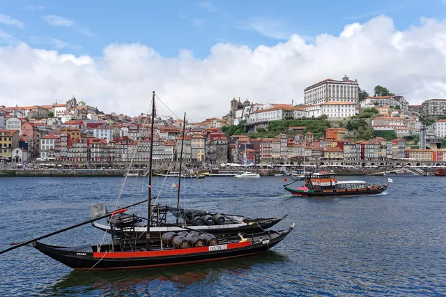 Traditional rabelo boats loaded with port barrels on the Douro, with the colourful Ribeira district of Porto rising behind