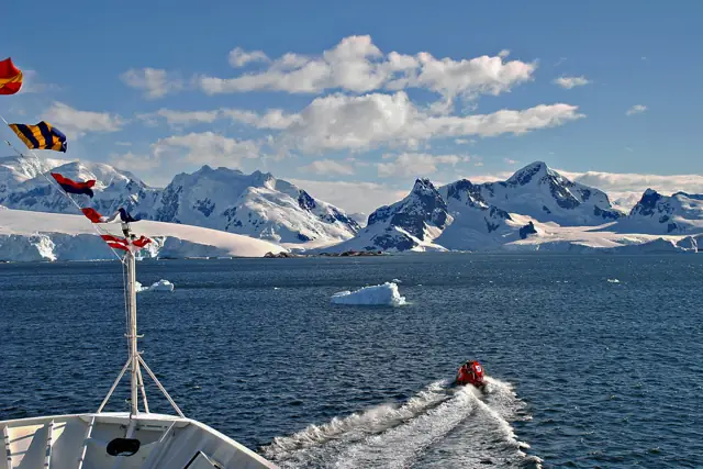 Expedition ship bow and a Zodiac crossing Paradise Bay with snow-covered mountains and icebergs on the Antarctic Peninsula