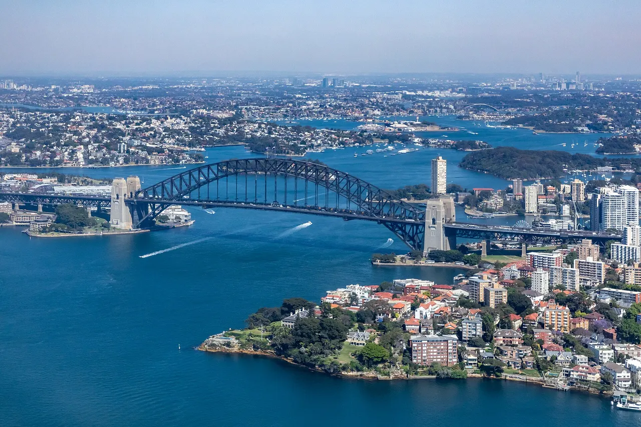 Aerial view of Sydney Harbour Bridge spanning the harbour, with the city and Kirribilli waterfront below