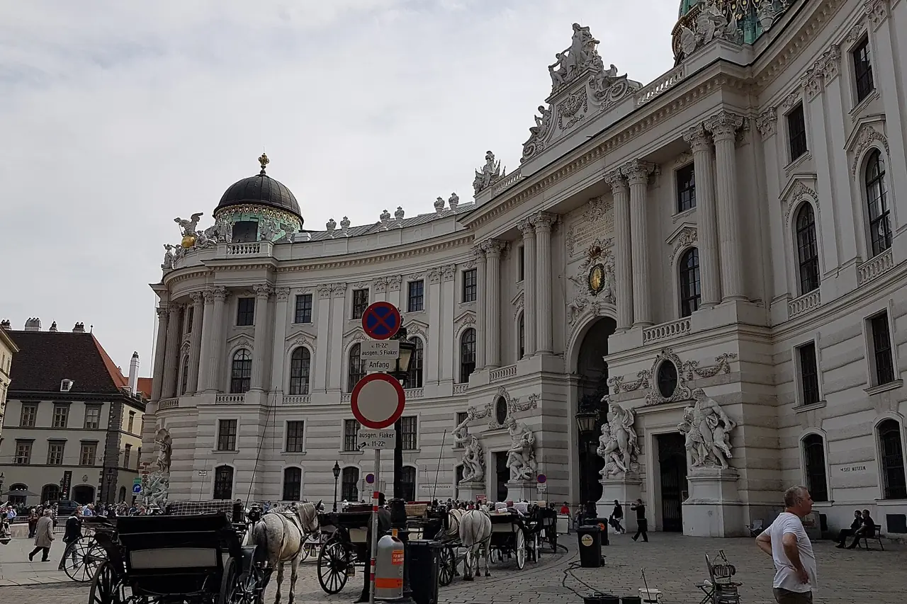 The curved Michaelertrakt facade of the Hofburg palace on Michaelerplatz in Vienna with horse-drawn carriages