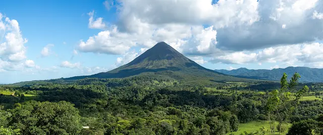 The cone of Arenal Volcano rising above green rainforest and farmland under a blue sky