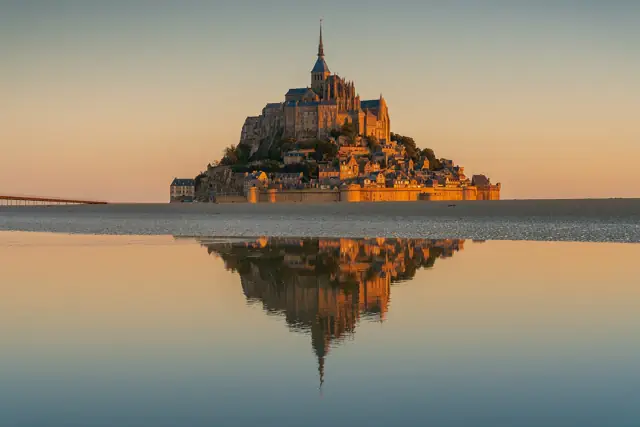 Mont-Saint-Michel abbey at sunrise reflected in the flooded tidal flats of the bay in Normandy