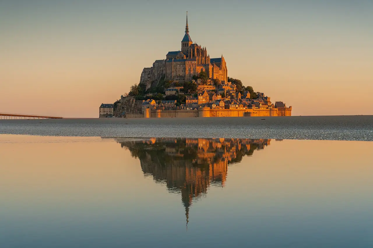Mont-Saint-Michel abbey at sunrise reflected in the flooded tidal flats of the bay in Normandy