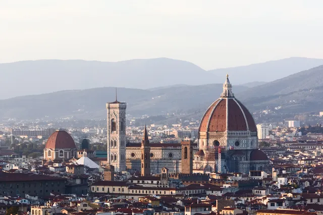 The red-tiled dome of Florence Cathedral and Giotto's bell tower rising above the rooftops, with Tuscan hills behind