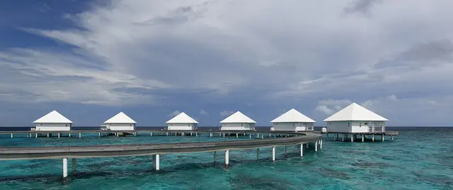 Overwater villas on stilts and a white-sand beach fringed by a turquoise lagoon at a Maldives resort