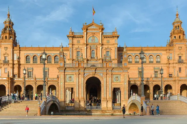 The curved brick and tile façade of Plaza de España in Seville with its towers and grand staircase under a blue sky