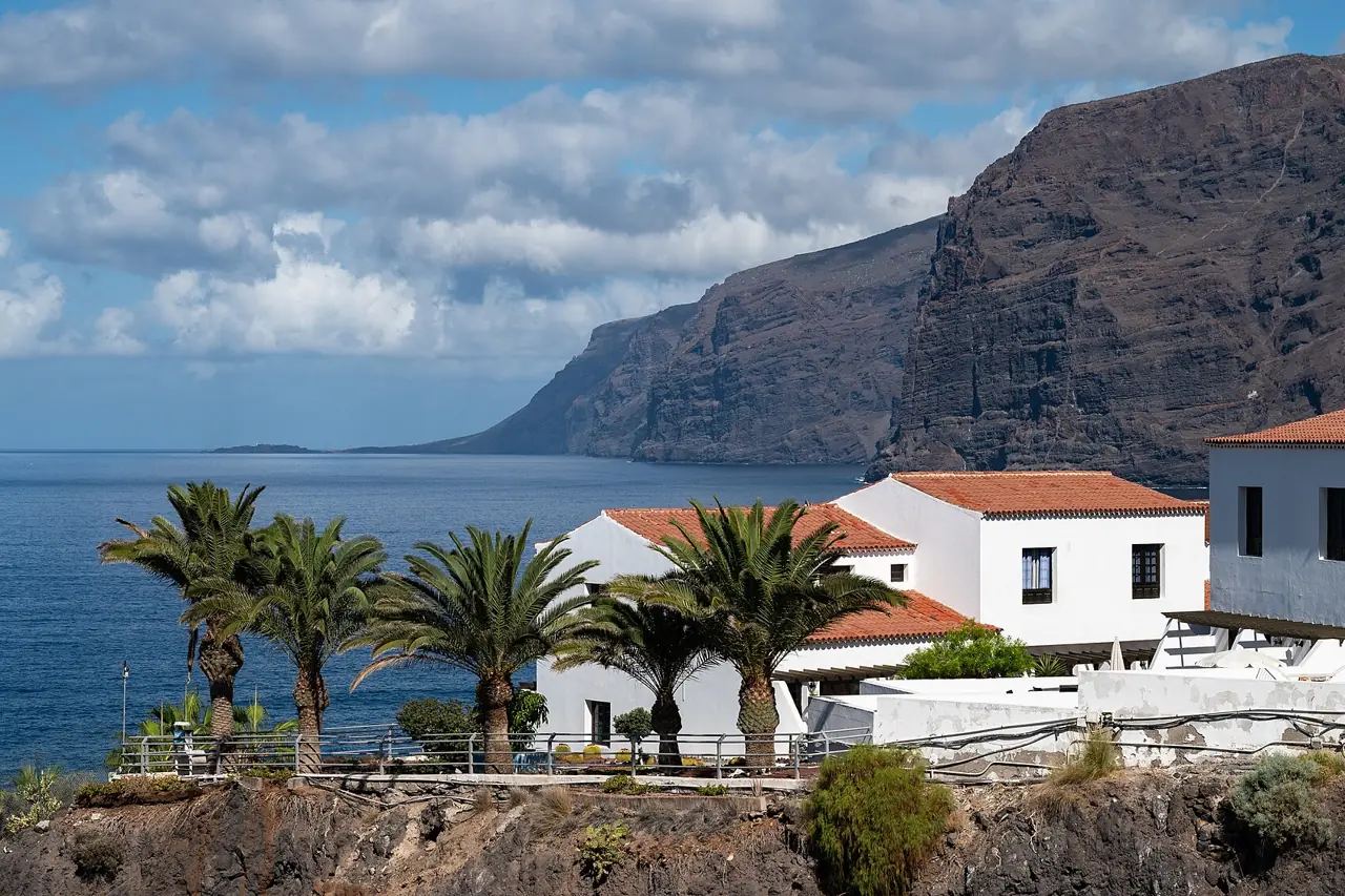 The sheer Los Gigantes cliffs rising from the sea behind palm trees and white houses on Tenerife's west coast