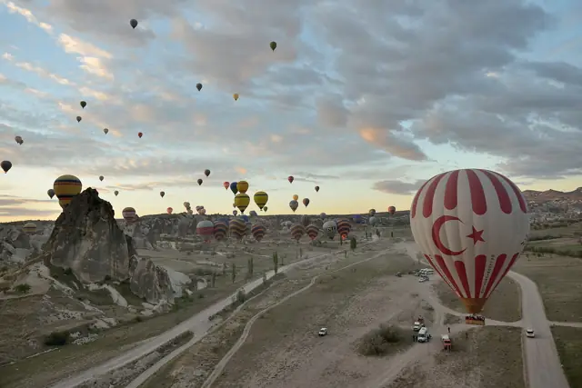 Hot-air balloons rising at dawn over the rock formations of Cappadocia near Uçhisar, with one balloon in the Turkish flag's colours