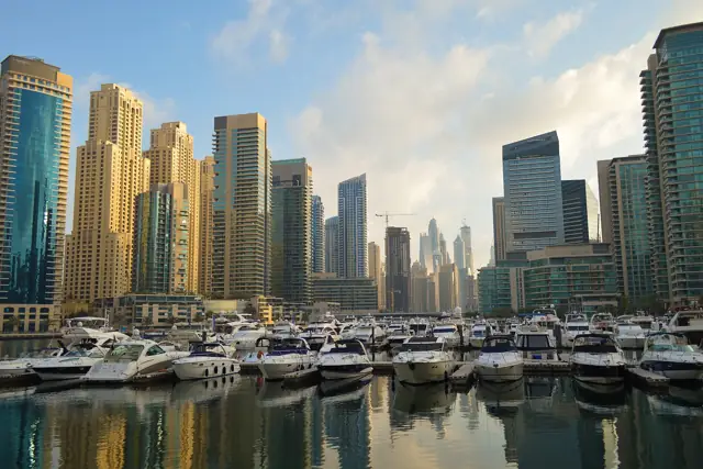 Skyscrapers of Dubai Marina rising above rows of moored yachts under a blue sky