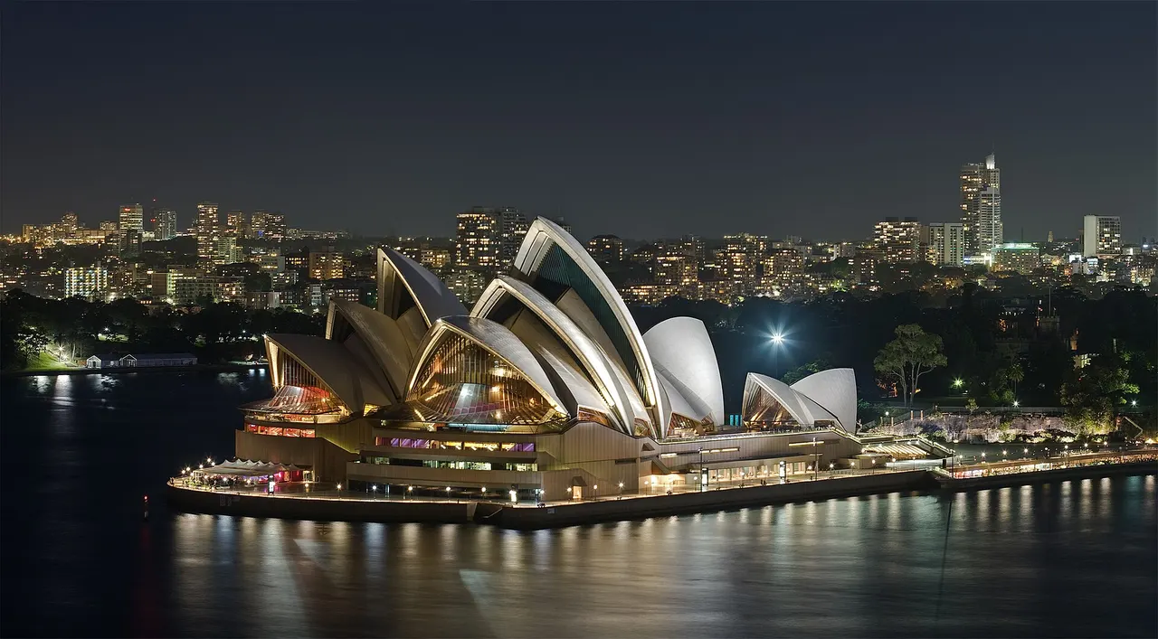 The Sydney Opera House lit up at night on Bennelong Point, with the city skyline behind